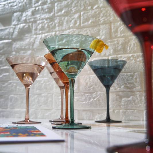 Set of colorful cocktail glasses on a bar counter with a light stone wall background.