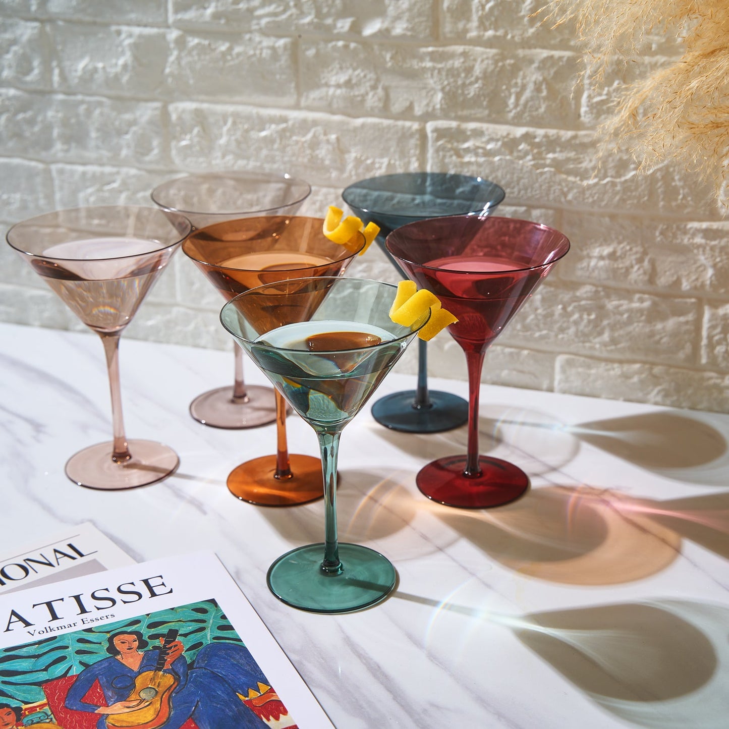 Set of colorful martini glasses on a table with a magazine underneath.