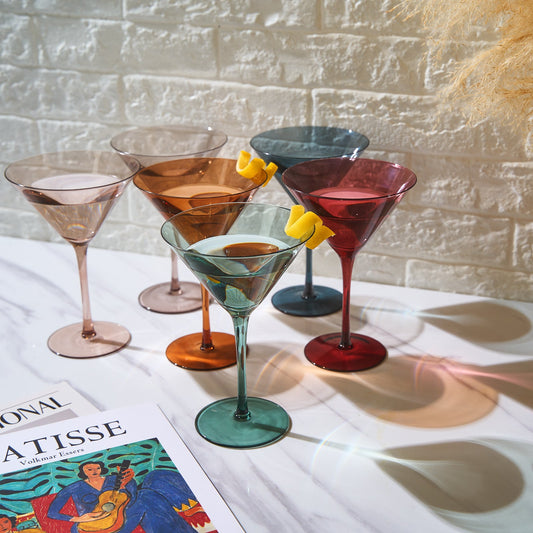 Set of colorful martini glasses on a table with a magazine underneath.